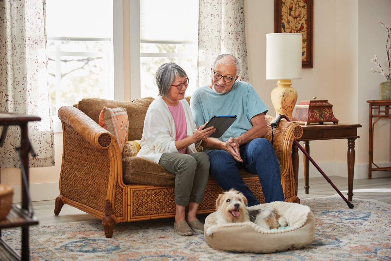 Senior couple sitting on couch together reviewing tablet with dog by their feet
