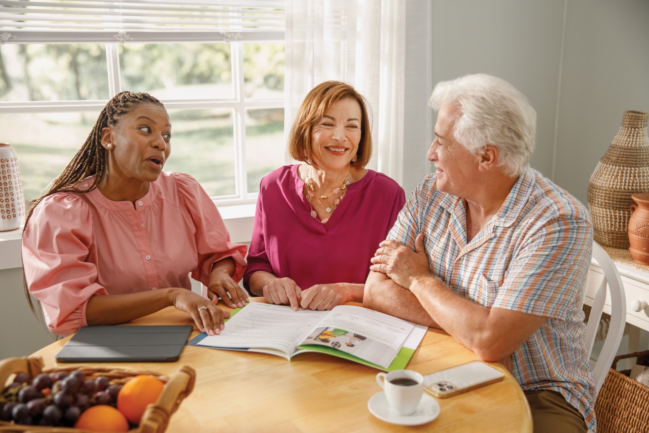 Senior couple reviews paperwork with agent together at kitchen table with coffee