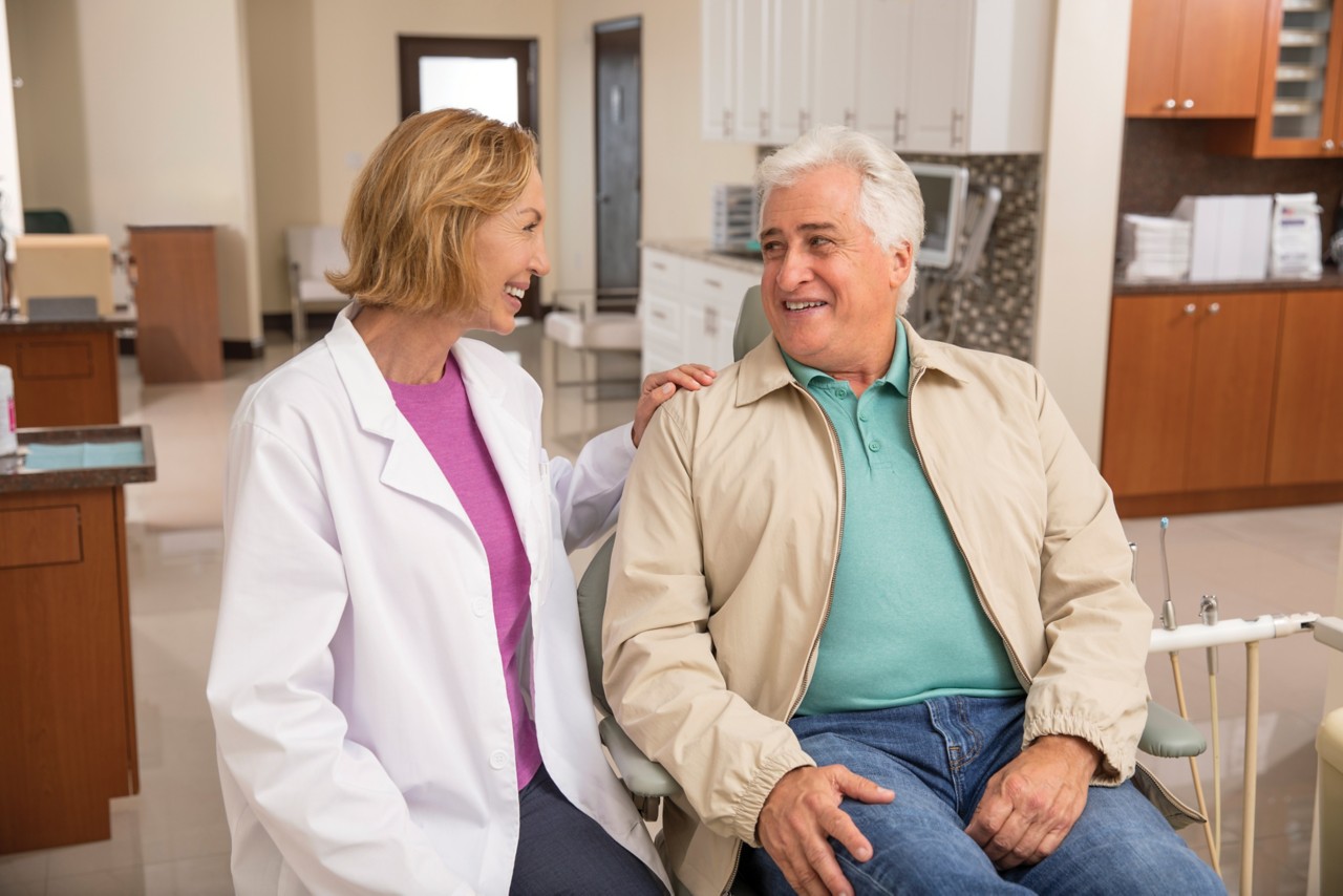 Senior man sitting in dentist chair getting ready for dental visit with female dentist