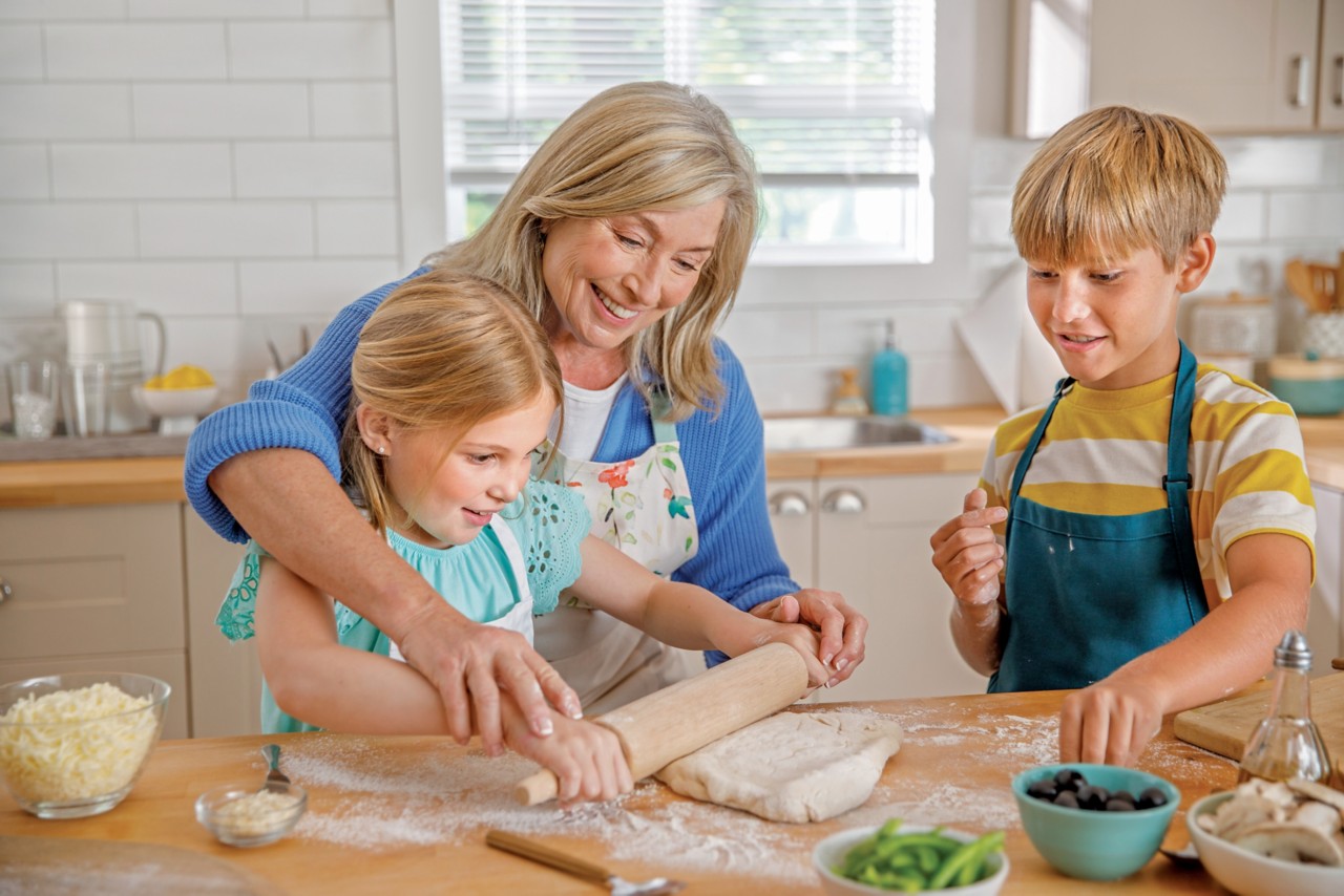 Senior woman cooks in the kitchen with her grandchildren, having fun together
